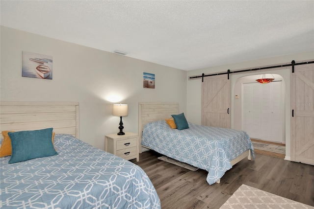 bedroom featuring dark wood-type flooring, a textured ceiling, a closet, and a barn door