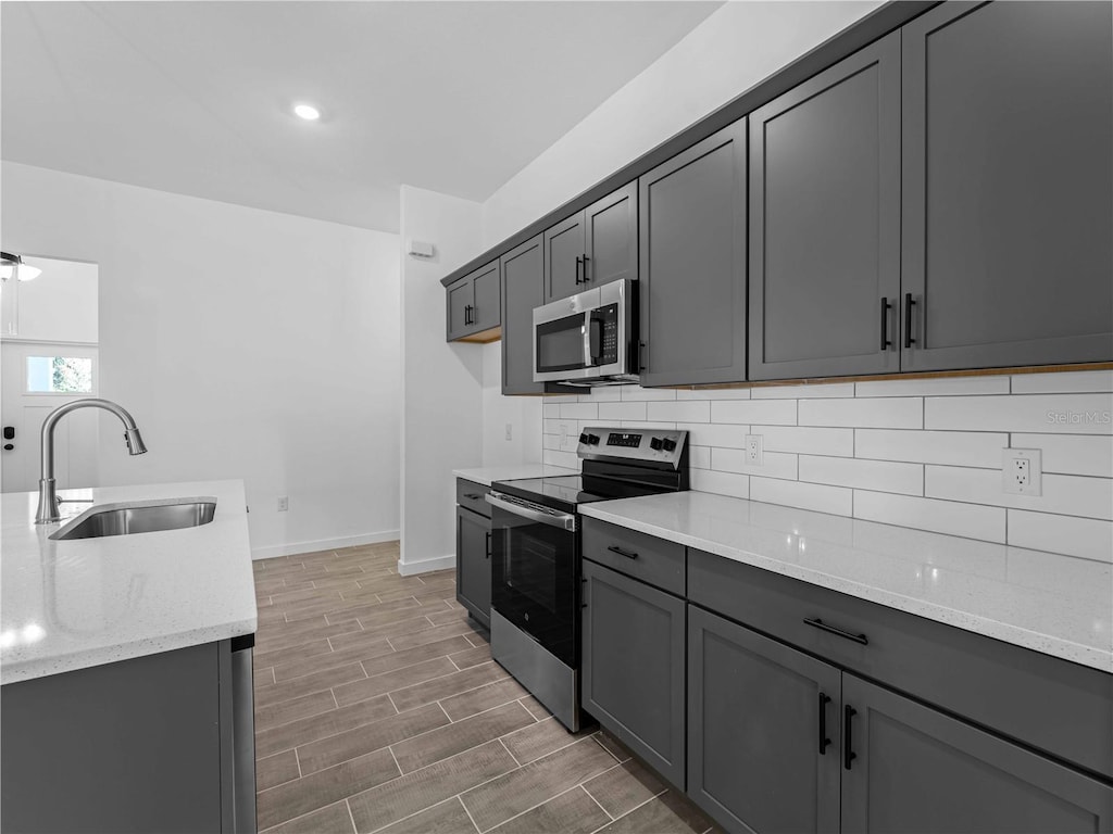 kitchen featuring stainless steel appliances, gray cabinetry, backsplash, light stone countertops, and sink