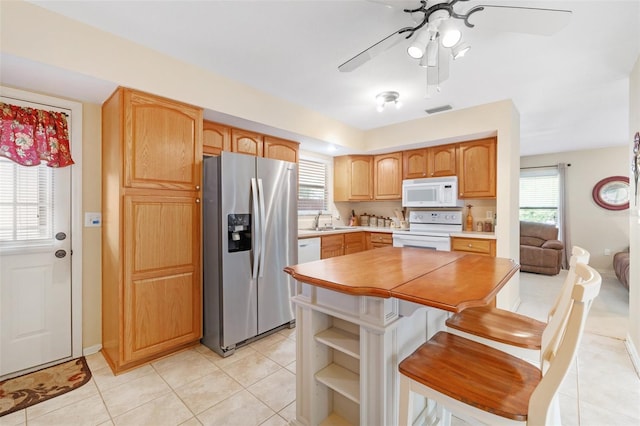 kitchen with white appliances, sink, ceiling fan, a breakfast bar area, and light tile patterned flooring