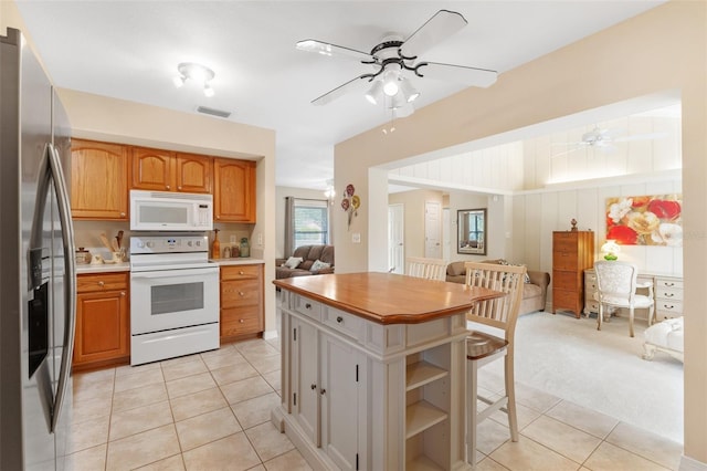 kitchen featuring a center island, white appliances, light carpet, ceiling fan, and a breakfast bar area