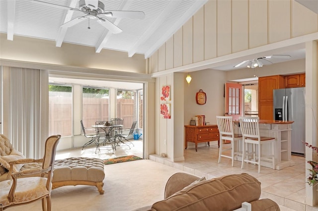 living room featuring ceiling fan, plenty of natural light, light tile patterned floors, and vaulted ceiling with beams