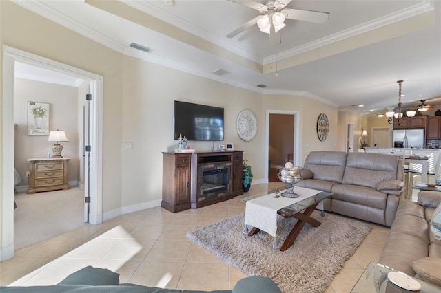 living room featuring ceiling fan with notable chandelier, light tile patterned floors, a tray ceiling, and crown molding