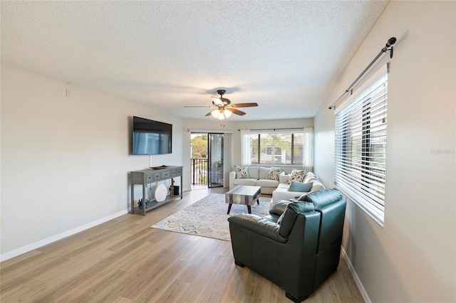 living room featuring ceiling fan, a textured ceiling, and light wood-type flooring