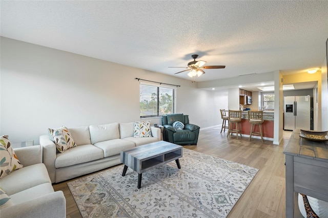 living room featuring ceiling fan, a textured ceiling, and light hardwood / wood-style floors