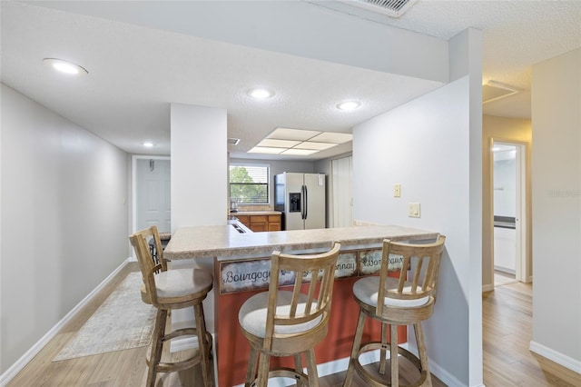 kitchen with stainless steel fridge, kitchen peninsula, a breakfast bar area, and light hardwood / wood-style flooring