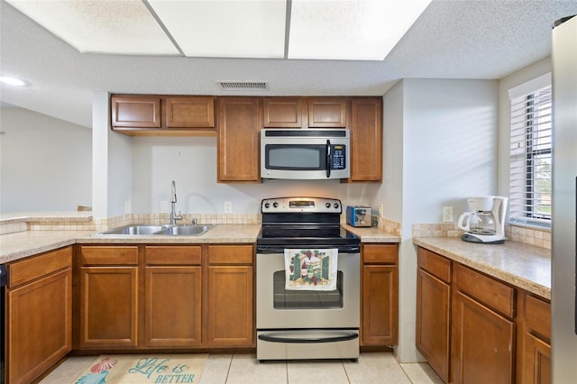 kitchen with light tile patterned flooring, appliances with stainless steel finishes, sink, and a textured ceiling