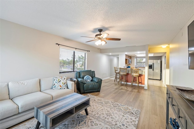 living room with a textured ceiling, ceiling fan, and light hardwood / wood-style flooring