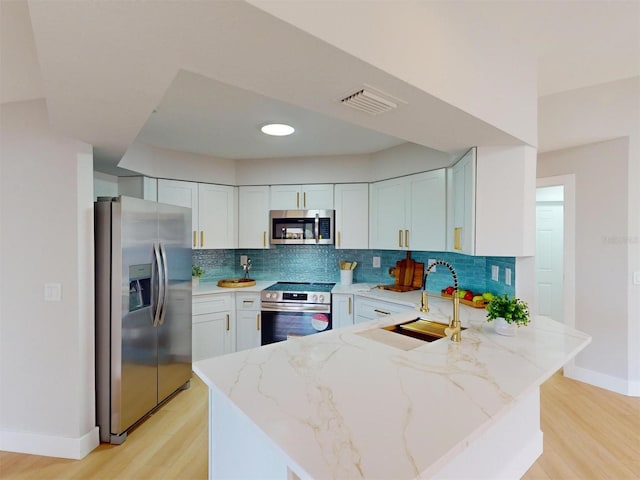 kitchen featuring appliances with stainless steel finishes, sink, tasteful backsplash, white cabinetry, and light stone countertops