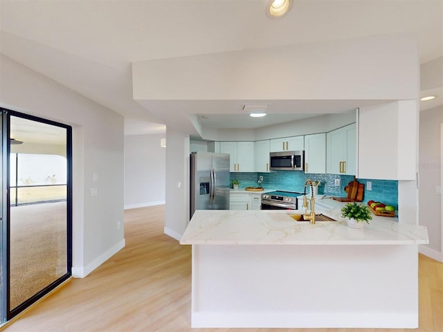 kitchen featuring kitchen peninsula, light wood-type flooring, light stone countertops, and appliances with stainless steel finishes