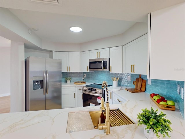 kitchen featuring white cabinets, stainless steel appliances, light stone counters, and tasteful backsplash