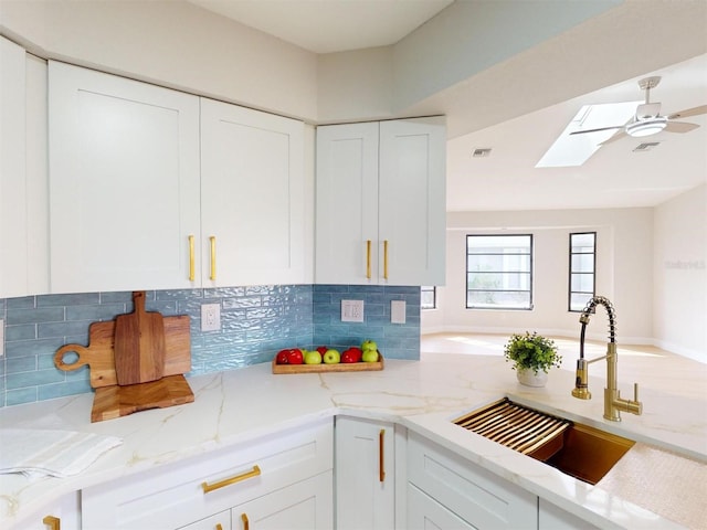 kitchen with light stone counters, sink, white cabinets, and a skylight