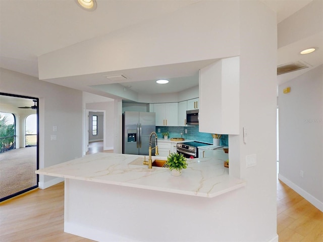 kitchen with kitchen peninsula, sink, white cabinets, light stone countertops, and stainless steel appliances