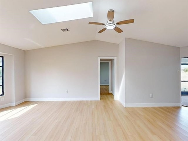 empty room featuring ceiling fan, vaulted ceiling with skylight, and light hardwood / wood-style flooring