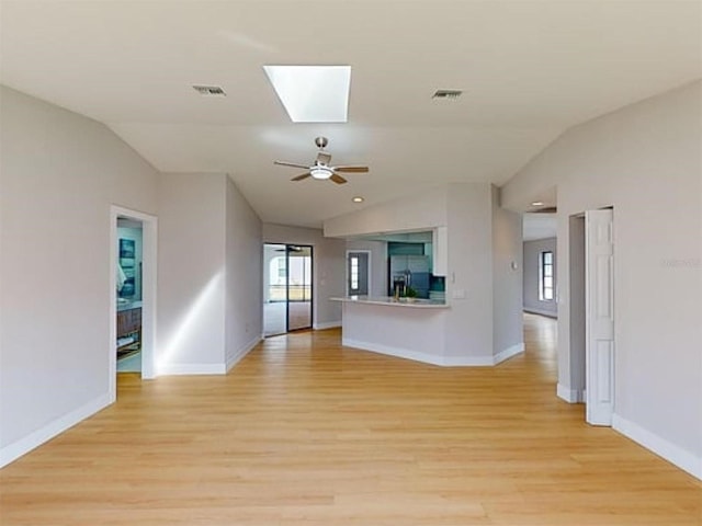 unfurnished living room featuring vaulted ceiling with skylight, a healthy amount of sunlight, and light wood-type flooring