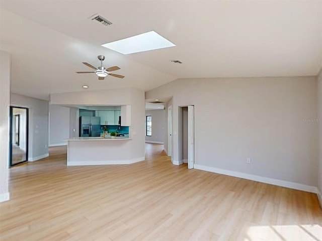 unfurnished living room featuring ceiling fan, lofted ceiling with skylight, and light hardwood / wood-style floors