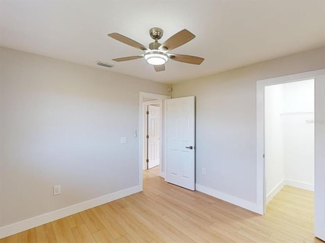 unfurnished bedroom featuring ceiling fan, light hardwood / wood-style floors, a closet, and a walk in closet