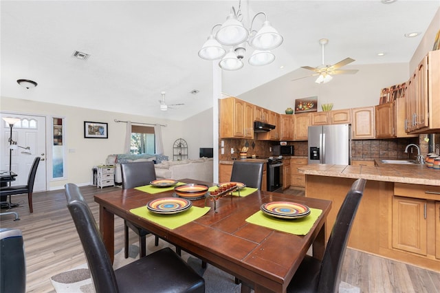 dining space featuring ceiling fan, high vaulted ceiling, sink, and light wood-type flooring