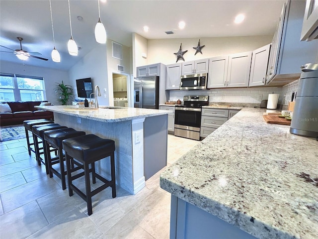 kitchen featuring gray cabinets, decorative light fixtures, lofted ceiling, backsplash, and stainless steel appliances