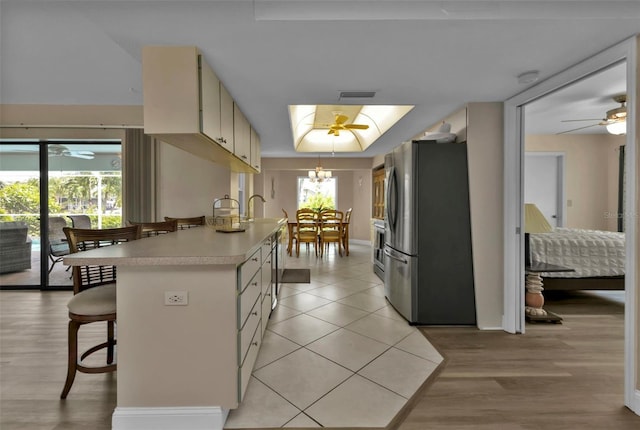 kitchen featuring appliances with stainless steel finishes, a kitchen breakfast bar, cream cabinets, ceiling fan, and light hardwood / wood-style flooring