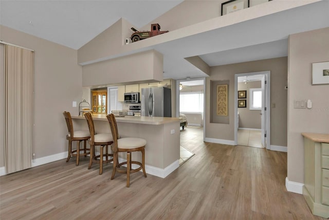 kitchen with a kitchen breakfast bar, light wood-type flooring, kitchen peninsula, and appliances with stainless steel finishes