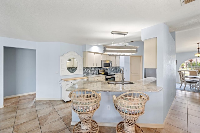 kitchen with kitchen peninsula, pendant lighting, appliances with stainless steel finishes, sink, and decorative backsplash