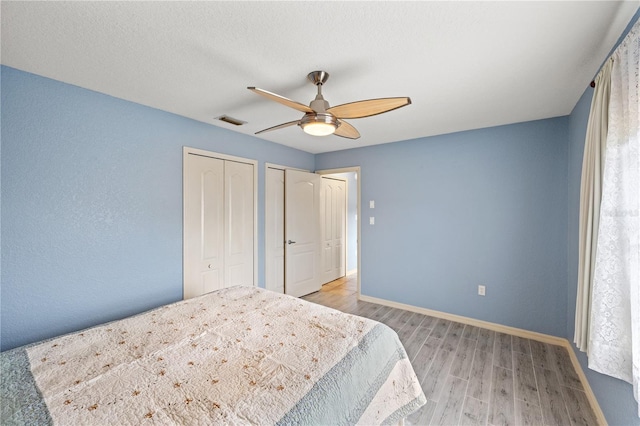 bedroom featuring ceiling fan, light wood-type flooring, and multiple closets