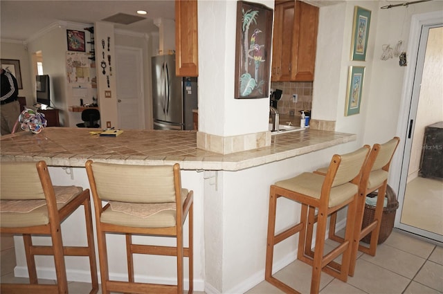 kitchen featuring stainless steel refrigerator, light tile patterned floors, decorative backsplash, a breakfast bar area, and tile countertops