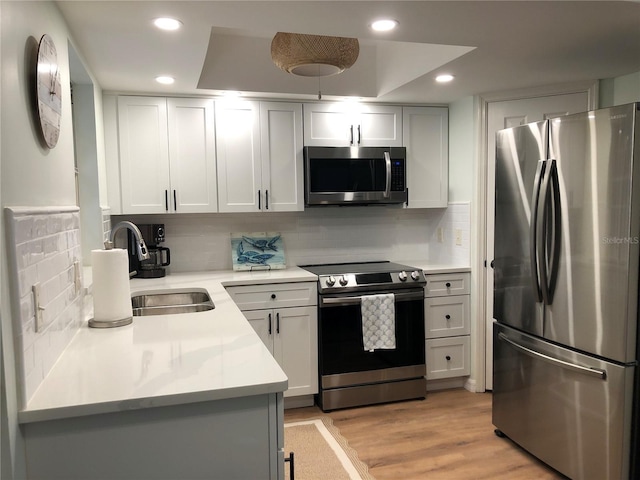 kitchen featuring white cabinetry, stainless steel appliances, light hardwood / wood-style floors, sink, and decorative backsplash