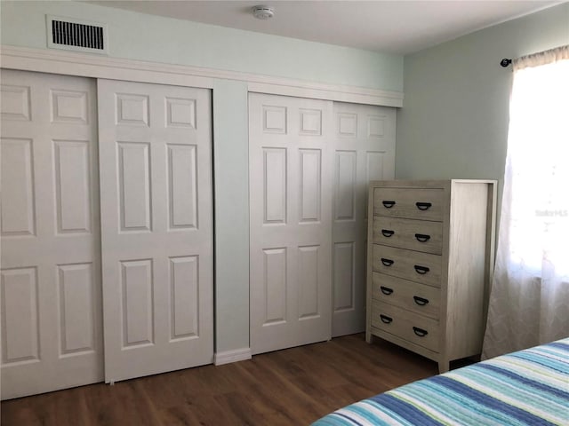 bedroom with multiple closets and dark wood-type flooring