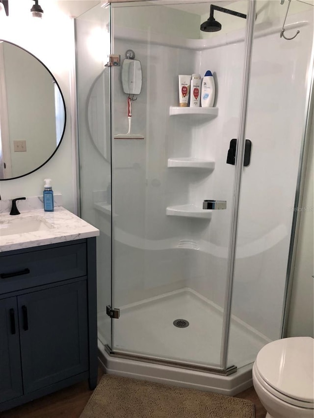 bathroom featuring a shower with door, toilet, and vanity