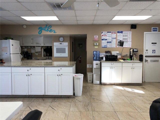 kitchen with white appliances, white cabinetry, a paneled ceiling, and light stone counters