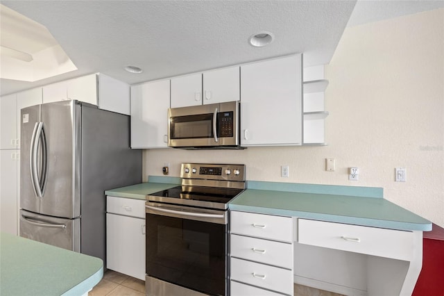 kitchen with light tile patterned flooring, a textured ceiling, appliances with stainless steel finishes, a tray ceiling, and white cabinets