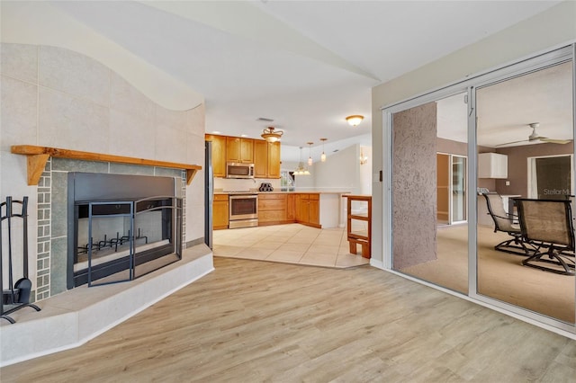 living room with vaulted ceiling, ceiling fan, a fireplace, and light hardwood / wood-style floors