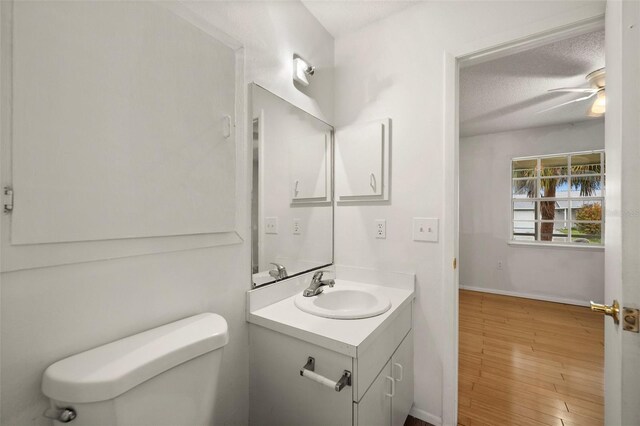 bathroom with toilet, a textured ceiling, wood-type flooring, vanity, and ceiling fan