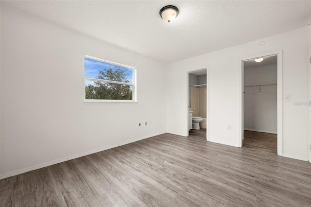 unfurnished bedroom featuring a spacious closet, a textured ceiling, wood-type flooring, a closet, and connected bathroom