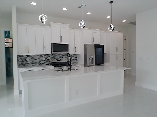 kitchen with stainless steel appliances, a center island with sink, white cabinets, and decorative light fixtures