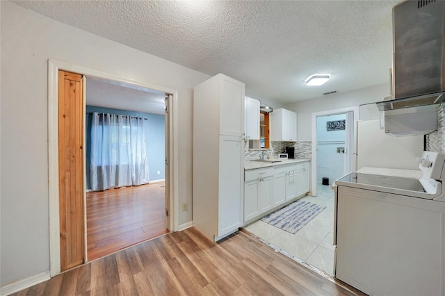 kitchen with washer / dryer, white cabinetry, a textured ceiling, light wood-type flooring, and backsplash