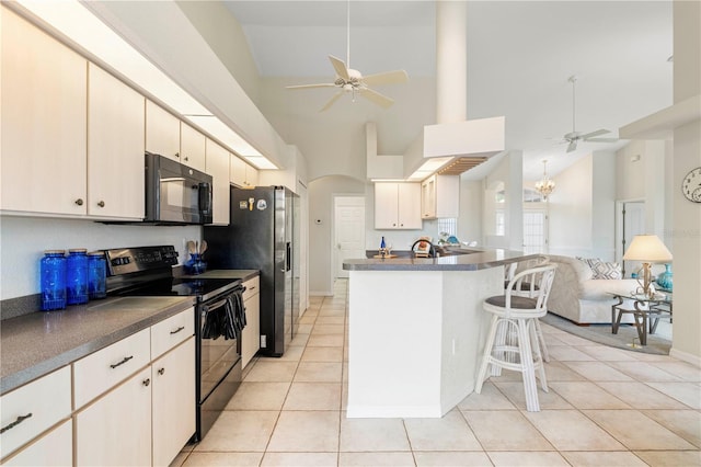 kitchen featuring black appliances, high vaulted ceiling, ceiling fan with notable chandelier, a breakfast bar area, and light tile patterned flooring