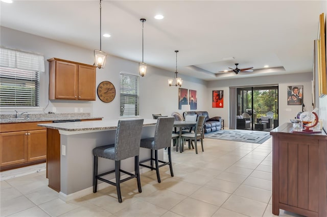 kitchen featuring a kitchen island, decorative light fixtures, light stone counters, a breakfast bar, and a tray ceiling