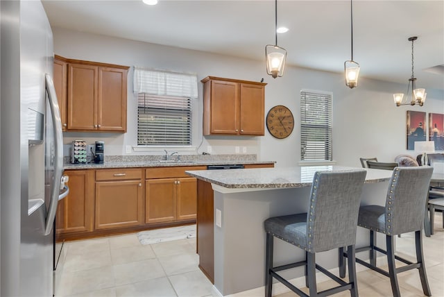 kitchen with a kitchen breakfast bar, stainless steel refrigerator with ice dispenser, pendant lighting, light stone countertops, and a kitchen island