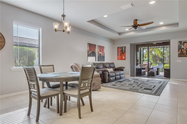 tiled dining area featuring ceiling fan with notable chandelier and a tray ceiling