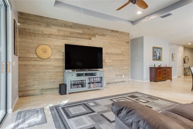 living room with ceiling fan, tile patterned flooring, a tray ceiling, and wooden walls