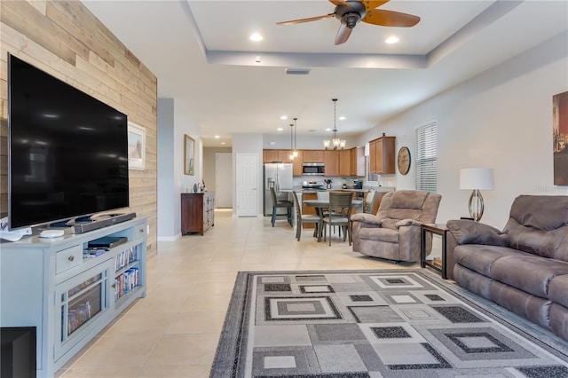 tiled living room featuring ceiling fan with notable chandelier and a tray ceiling