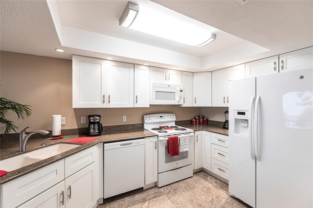 kitchen with white appliances, white cabinets, dark stone countertops, sink, and a tray ceiling