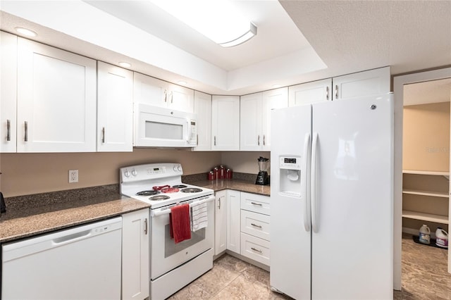 kitchen with white appliances, white cabinetry, dark stone counters, and a raised ceiling