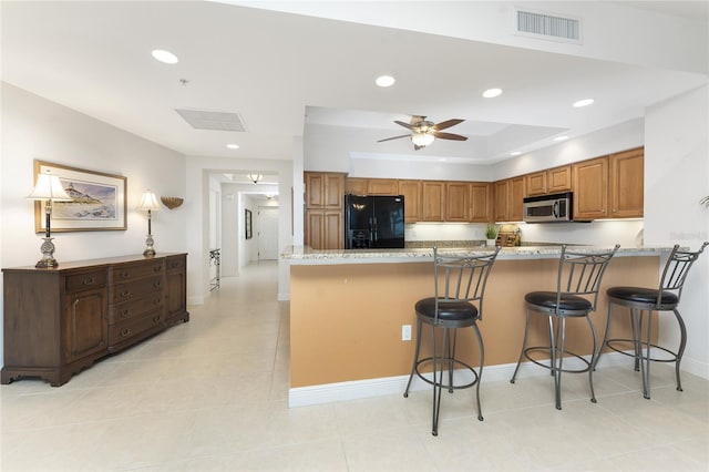 kitchen with light stone counters, a breakfast bar, black fridge with ice dispenser, and kitchen peninsula