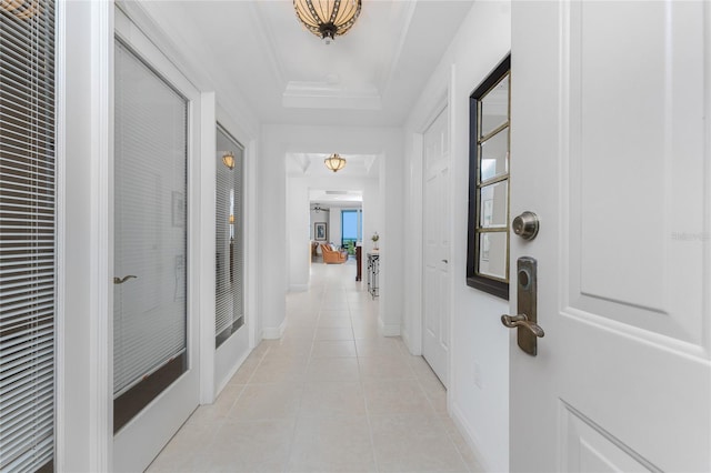 hall featuring light tile patterned flooring, a tray ceiling, and crown molding