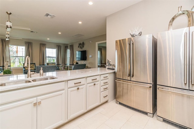 kitchen with stainless steel refrigerator, white cabinetry, light stone countertops, and sink