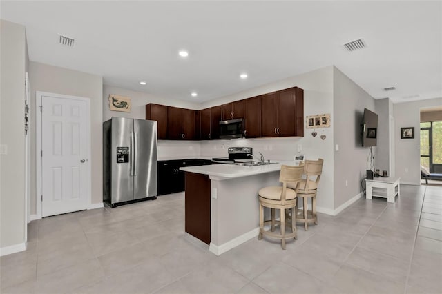 kitchen with light tile patterned floors, a breakfast bar area, appliances with stainless steel finishes, dark brown cabinetry, and kitchen peninsula