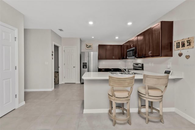 kitchen with sink, dark brown cabinets, a kitchen breakfast bar, kitchen peninsula, and stainless steel appliances